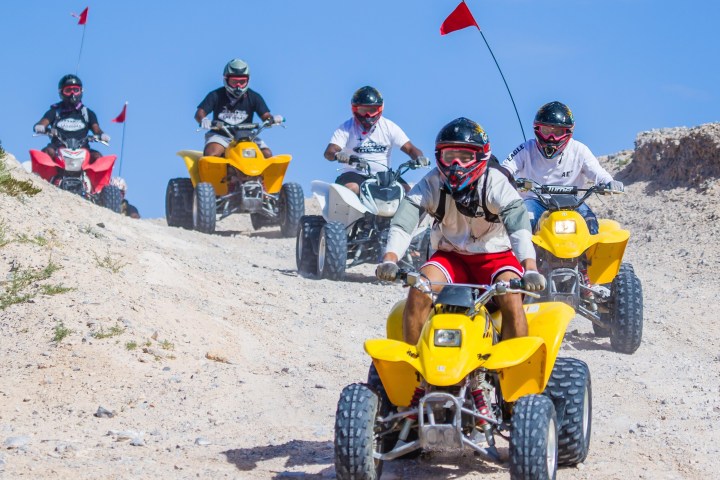 Five people riding ATVs on a dirt trail under clear blue sky.