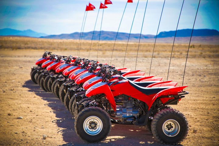 Line of red ATVs with flags in a desert landscape.