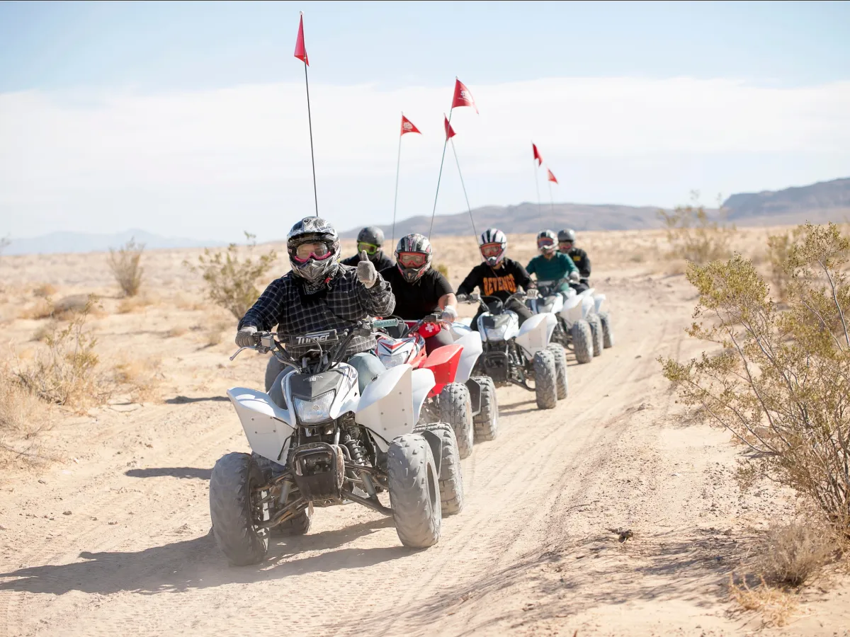 Group of people riding ATVs in desert terrain with red flags on poles.