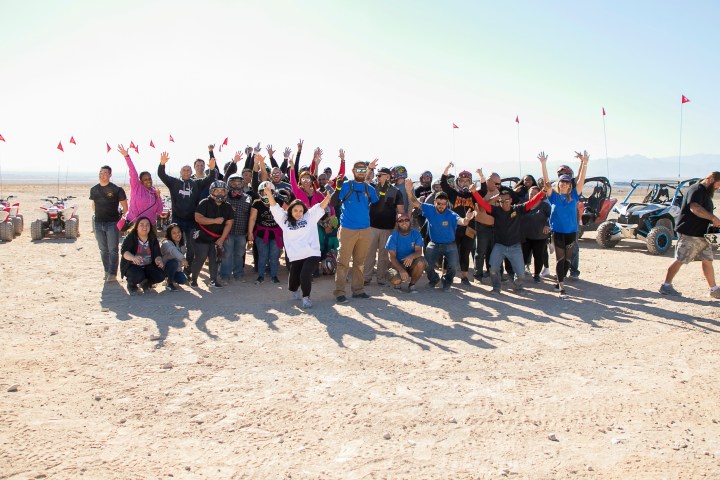 Group of people posing and cheering in the desert with off-road vehicles.