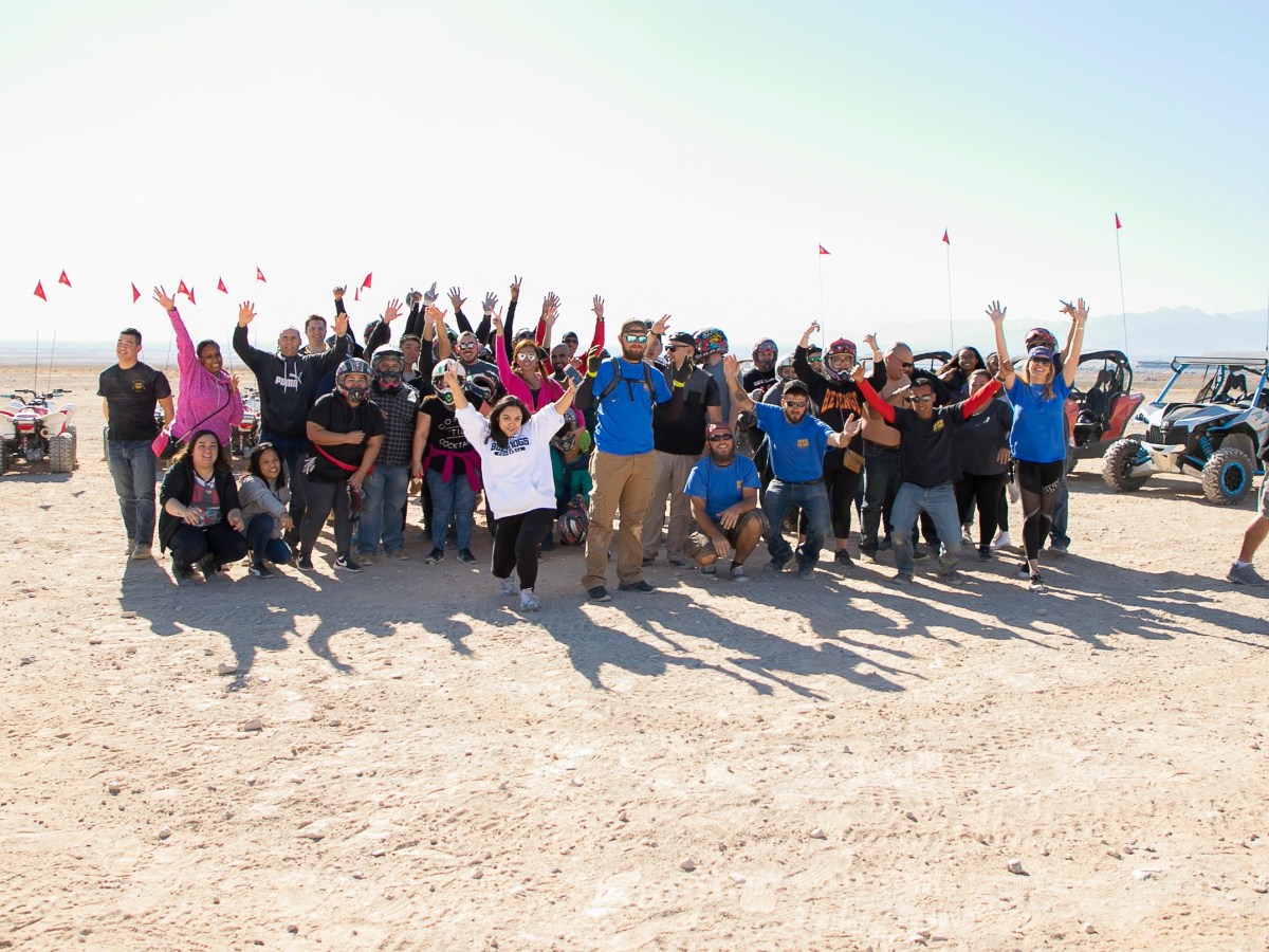 Group of people posing and cheering in the desert with off-road vehicles.