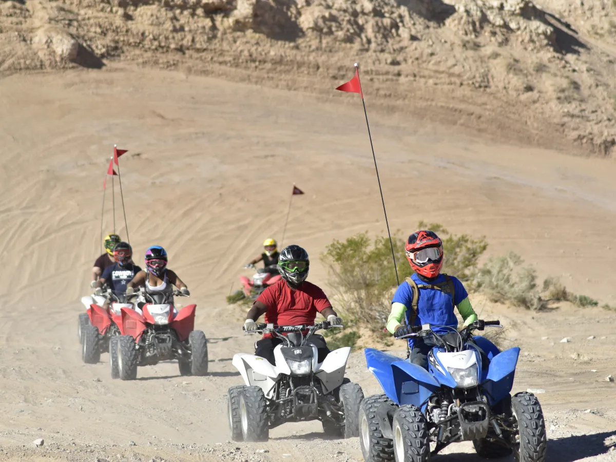 Group of people riding ATVs on a desert trail with rocky terrain.