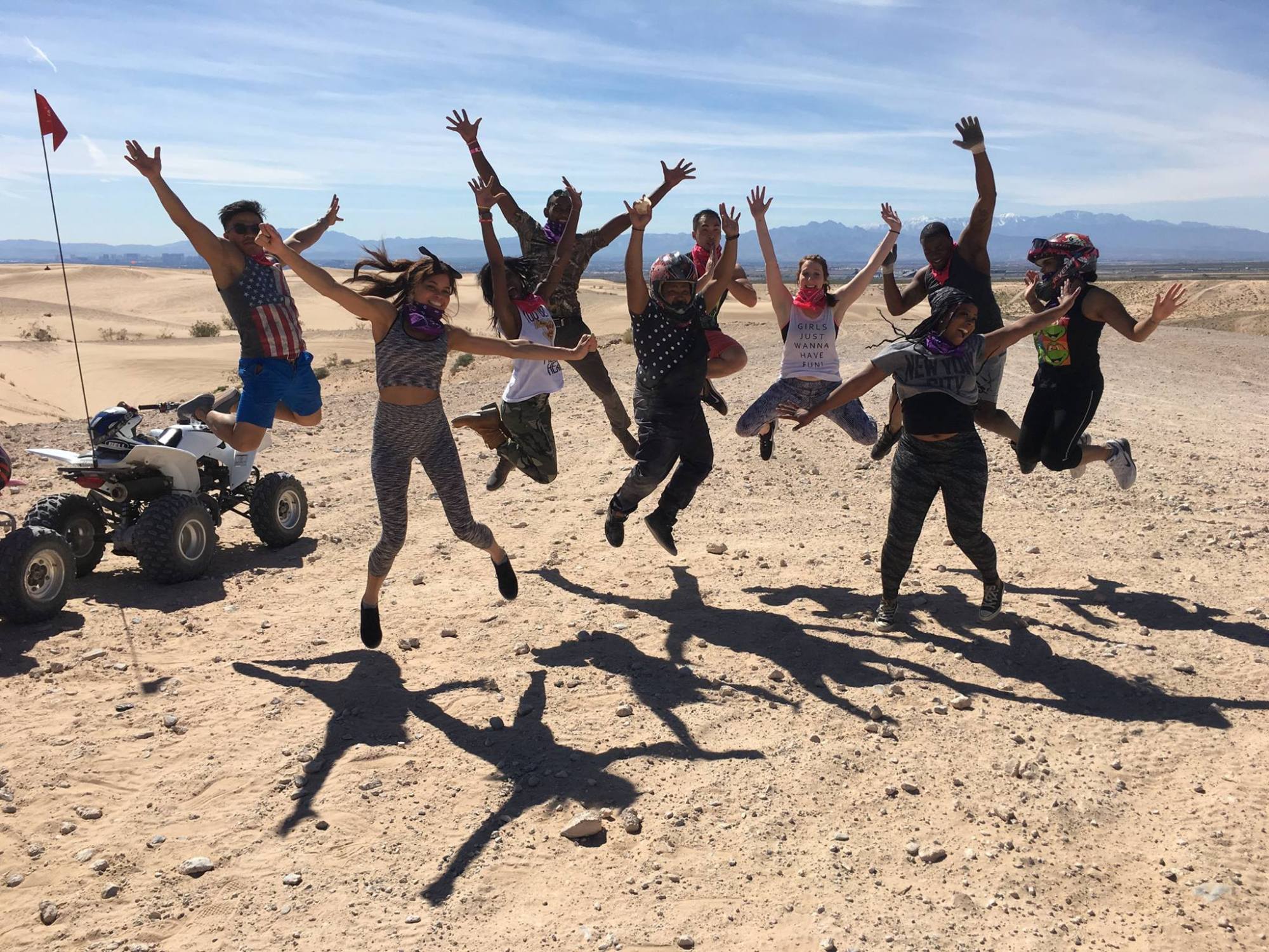 Group of people jumping with joy in a desert, quad bike in the background.