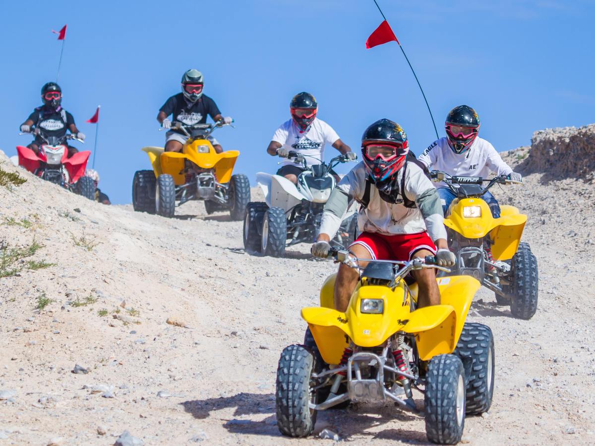 Five people riding quad bikes on a rocky terrain, wearing helmets and goggles.